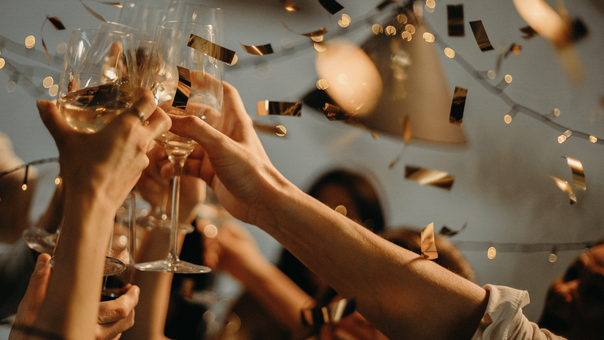 Guests raising wine glasses for a toast beneath falling gold confetti and string lights.
